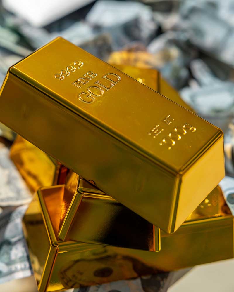 Goldbarren mit der Aufschrift Fine Gold, gestapelt vor Geldscheinen
